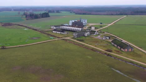 Aerial-view-circling-various-farm-buildings-with-steel-silo-containers-on-rural-agricultural-farmland