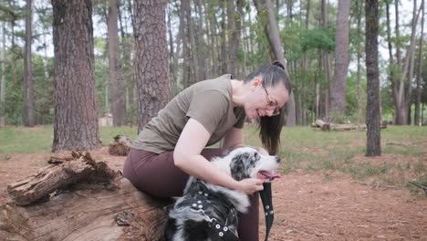 Woman-sitting-on-a-tree-trunk-petting-her-Australian-Shepherd-dog
