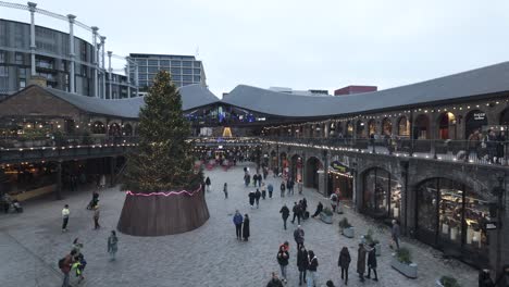 Festive-Large-Christmas-Tree-At-Coal-Drops-Yard-In-Kings-Cross-With-Shoppers-Walking-Past-On-Overcast-December-Day