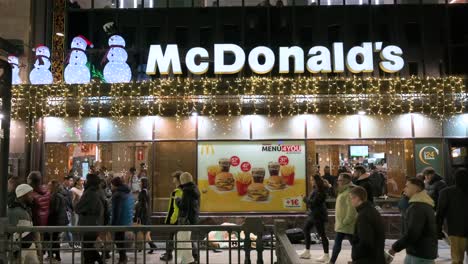People-walk-past-the-American-multinational-fast-food-hamburger-restaurant-chain,-McDonald's,-decorated-with-Christmas-lights