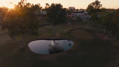 aerial-drone-shot-of-a-golf-hole-with-a-fountain-and-pond-during-sunrise