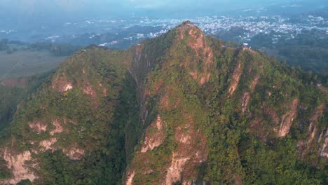 Vista-De-Drones-En-Guatemala-Volando-Frente-A-Una-Montaña-Verde-Rodeada-De-Volcanes-Al-Amanecer-En-Atitlán