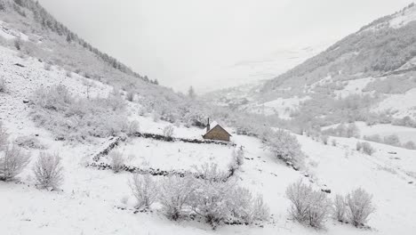 Aerial-shot-of-a-lonely-snowy-rustic-house-in-the-middle-of-the-mountains-of-a-valley-in-the-Spanish-Pyrenees-on-a-cloudy-day