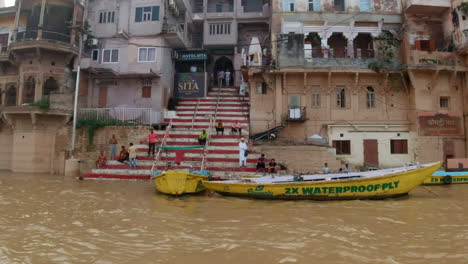 Cinematic-slow-motion-stairs-to-Varanasi-India-Ganges-River-cruise-canal-boats-Northern-State-gathering-Ancient-Holy-city-Ghat-Pradesh-Province-landscape-gray-cloudy-afternoon-muddy-brown-left