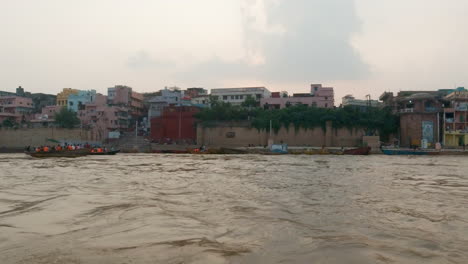Filmische-Ganges-Fluss-Chowk-Menschen-Auf-Kreuzfahrt-Kanalboot-Varanasi-Nordindien-Bundesstaat-Alte-Heilige-Stadt-Khidkiya-Ghat-Pradesh-Provinz-Landschaft-Grau-Wolkig-Heilig-Schlammig-Braun-Bewegung-Nach-Links-Folgen