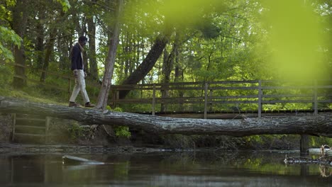 Black-man-crossing-a-creek-on-tree-trunk-bridge-in-the-woods---left-to-right