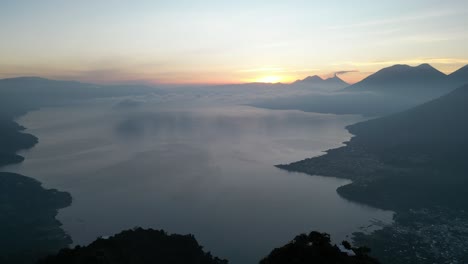 Vista-De-Drones-En-Guatemala-Volando-De-Regreso-Desde-Un-Lago-Azul-Rodeado-De-Verdes-Montañas-Y-Volcanes-En-Un-Día-Nublado-En-Atitlán