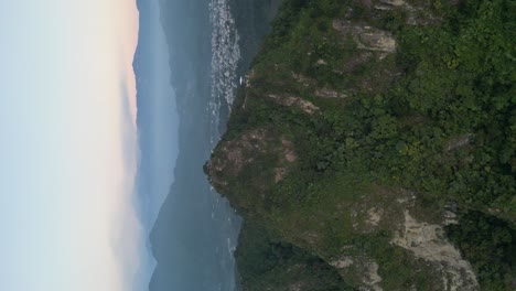 Drone-portrait-view-in-Guatemala-flying-in-front-of-a-green-mountain-surrounded-by-volcanos-on-a-cloudy-day-in-Atitlan
