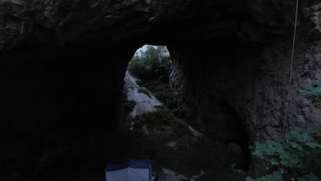 aerial-drone-shot-entering-a-dark-and-mysterious-cave-surrounded-by-vegetation