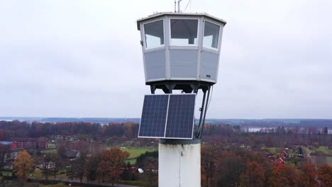 Old-firefighter-lookout-tower-with-solar-panel-installation-aerial-view-descending-pole-to-autumnal-countryside-landscape