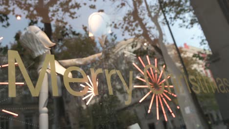 Commemorating-the-Christmas-season,-a-sticker-on-a-glass-window-with-LED-fireworks-animation-in-the-background-is-seen-at-a-fashion-retail-shop-with-the-message-"Merry-Christmas"