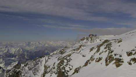 Drohne-Fliegt-In-Der-Nähe-Des-Schneebedeckten-Berges-In-Richtung-Rifugio-Quintino-Sella-Al-Felik,-Mit-Den-Alpen-Und-Dem-Mont-Blanc-Massiv-Im-Hintergrund-Im-Hintergrund