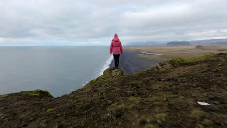 Female-Standing-On-Edge-Of-The-Cliff-At-Dyrhólaey-Viewpoint-In-Iceland---Aerial-Pullback