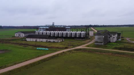 Various-farm-buildings-aerial-view-rising-overlooking-shiny-steel-silo-containers-on-rural-agricultural-farmland