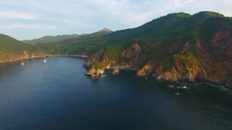 Drone-video-sliding-along-the-rough-terrain-at-Carrizal-anchorage-by-Manzanillo-Mexico-at-sunset-overlooking-sailboats-anchored-in-the-bay