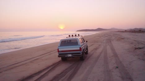 Following-ford-Bronco-vehicle-driving-across-sandy-Pacific-ocean-beach-at-sunset-in-Oaxaca