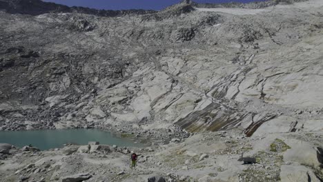Hikers-by-a-glacial-lake-with-water-flowing-on-uniquely-shaped-granite,-Neves-Nofesferner-glacier-afar