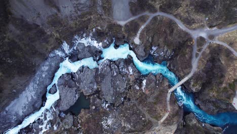 Stunning-wild-blue-river-and-waterfall-Barnafoss-in-volcanic-landscape,-aerial-top-down-panorama