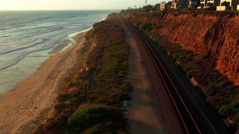 Aerial-shot-tracks-cyclist-riding-along-the-bluffs-in-Del-Mar,-CA-at-sunset