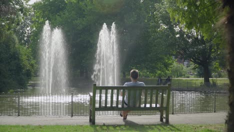 Ein-Mann,-Der-Im-Sommer-Auf-Einer-Parkbank-Vor-Einem-Wasserbrunnen-Im-Leamington-Spa-Sitzt
