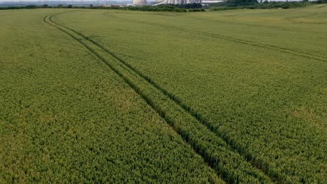 Aerial-drone-flying-over-agricultural-fields-of-barley-with-a-lift-to-reveal-a-large-coal-powered-power-station
