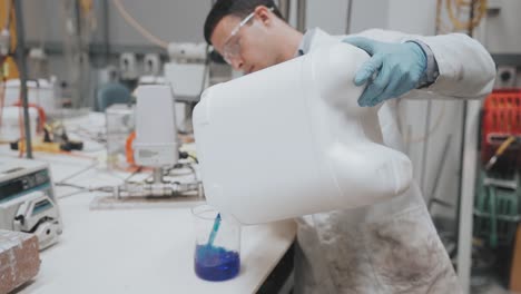 Wissenschaftler-Kippt-Blaue-Flüssigkeit-In-Ein-Becherglas-In-Einem-Labor