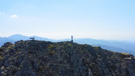Cinematic-aerial-drone-shot-of-man-stood-at-the-very-top-of-the-Troodos-mountains,-Cyprus