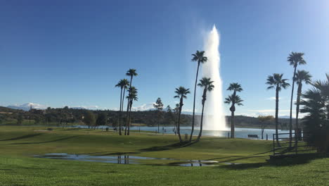 Large-water-fountain-in-a-desert-park-with-palm-trees-surrounding-the-lake