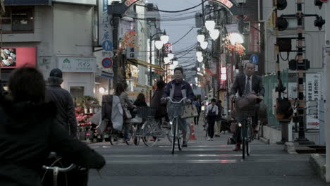 Blick-Auf-Die-Straße-Eines-Tokioter-Stadtmarktes,-In-Dem-Menschen-An-Einem-Späten-Abend-Mit-Ihren-Fahrrädern-Die-Straße-überqueren