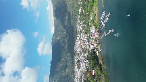 Drone-portrait-view-in-Guatemala-flying-over-a-blue-lake-surrounded-by-green-mountains-and-volcanos-on-a-sunny-day-in-Atitlan