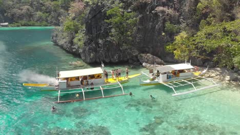 Aerial-Drone-shot-away-from-people-enjoying-life-on-Paraw-boats,-on-a-Philippine-tour,-over-clear-blue-water-and-paradise-islands,-at-Coron-isle,-in-Philippines,-Asia