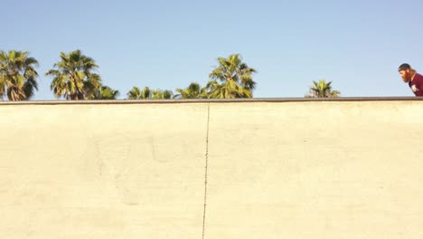 Slow-motion-of-male-in-baseball-cap-sliding-the-side-of-skate-park-bowl,-casting-shadow-on-wall