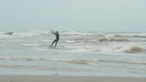 Man-kitesurfing-at-the-beach-of-East-Galveston,-high-waves,-on-a-cloudy-day,-wide-shot
