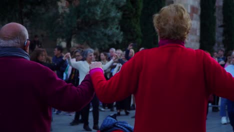 Panning-Shot,-Elderly-People-Holding-Hands-in-Traditional-Dance-Sardana-in-Plaza-Nova,-Barcelona,-Spain,-Elderly-People-in-the-background