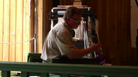 Male-glassblower-in-workshop-rotating-and-shaping-a-piece-of-glass