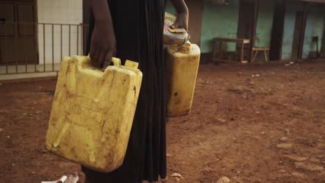 Barfüßiges-Ugandisches-Mädchen,-Das-Während-Des-Sonnenaufgangs-In-Einem-Ländlichen-Dorf-Zwei-Gelbe-Wasserbehälter-Hält