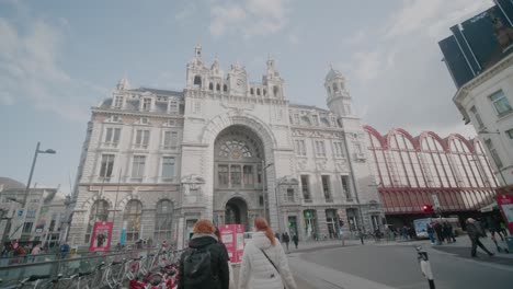 Young-Women-Approach-Antwerp-Central-Railway-Station,-Past-Hire-Bikes