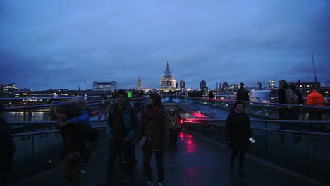 People-Walking-At-Millennium-Bridge-In-London,-United-Kingdom-With-The-Ancient-Saint-Paul's-Cathedral-In-The-Background-At-Night---Wide-Shot