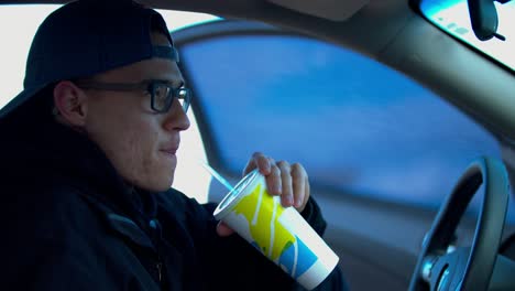 Dieses-Video-Zeigt-Einen-Mann-Mit-Blauer-Mütze-Und-Schwarzer-Brille,-Der-In-Einem-Auto-Limonade-Trinkt