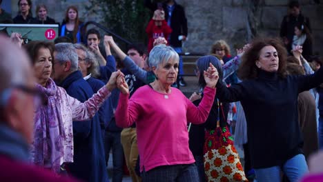 Panning-Shot,-Elderly-Women-Holding-Hands-While-Dancing-in-a-Traditional-Dance-Sardana-in-Plaza-Nova,-Barcelona-Spain