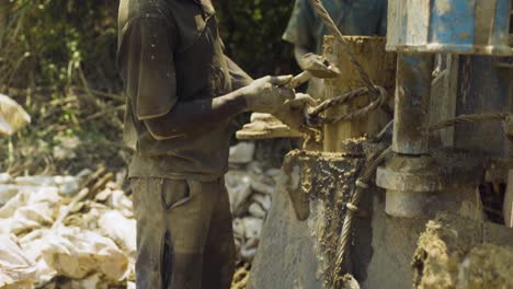 Afrikanischer-Bauarbeiter,-Der-Mit-Einem-Hammer-Ein-Rohr-Für-Einen-Neuen-Brunnen,-Den-Sie-Bauen,-Festhält