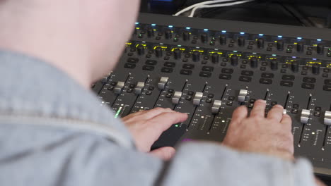 An-audio-engineer-operating-on-an-audio-mixer-filmed-from-an-over-shoulder-perspective