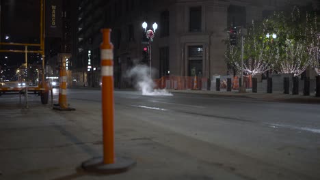 Cars-Drive-Through-Steam-from-City-Manhole-near-Construction-at-Night