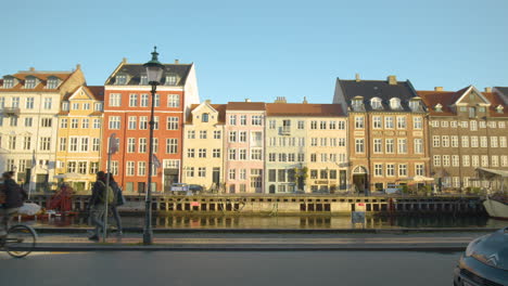 Famous-Danish-landmark-of-Nyhavn-colorful-houses-in-Copehagen,-people-and-bike-goes-past