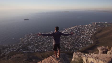 Man-raising-hands-above-the-spectacular-view-of-Cape-Town-on-top-of-the-Lions-Head-Mountain-in-Slow-Motion