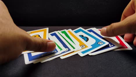 Nahaufnahme-Männlicher-Hände,-Die-Nacheinander-Ein-Paar-Uno-Spielkarten-Auf-Einem-Schwarzen-Tisch-Ausbreiten
