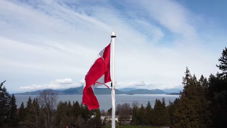 Bright-red-Canadian-flag-flapping-in-the-wind-with-an-ocean-and-mountain-backdrop