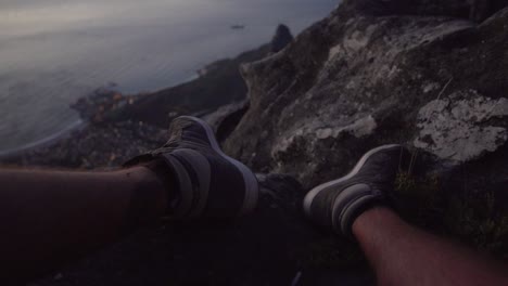 View-of-Cape-Town-and-Lions-Head-at-night-from-Table-Mountain-above-a-mans-feet,-in-Slow-Motion