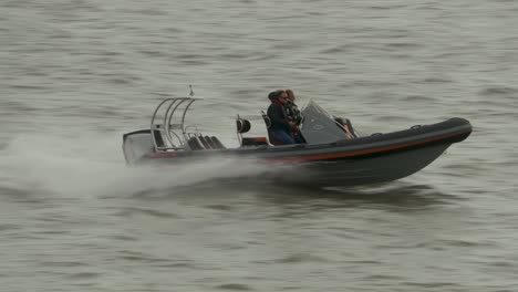 Two-people-in-a-Rigid-Inflatable-boat-motoring-across-a-cold-grey-choppy-sea-and-waves