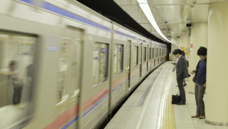 Pendler-Warten-In-Einer-U-Bahn-Station-In-Tokio-Auf-Einen-Zug,-Der-In-Den-Bahnhof-Einfährt